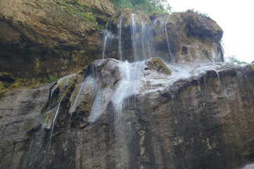 a small waterfall in the mountains with crystal clear water the mountain is covered with forest with green trees on a fine summer day