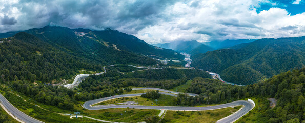 panorama of a mountain road, serpentine descending down a forested slope to the valley of the...