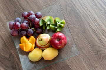 Composition with fresh mixed fruits on plate.Assortment of juicy fruits on wooden table.Fruit platter with fresh grapes, apple, kiwi, orange. Fruit tray as healthy food for party and holidays table.
