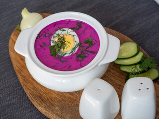 Close-up of cold chlodnik soup on a wooden board. Soup of Polish Belarusian and Russian cuisine made of beetroot and kefir, decorated with half an egg. Healthy food.