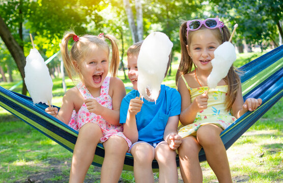 Happy Childhood. Cheerful Kids Eating The Sugar Cotton Candy And Laughing.