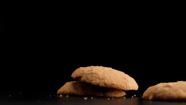 Super slow motion of stack of cookies falling on table on black background.