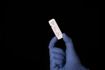 Hand with glove holding a COVID-19 Antigen Rapid Test Kit showing positive result over black background