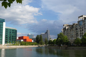 Obraz premium Office and residential buildings on Dambovita river shores in sunny day in Bucharest. Romanian Chamber of Commerce and Industry in center, National Operetta Theater (red) and National Library (on left