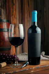 bottle of red wine with very elegant glass filled with wine and wooden barrel in the background
