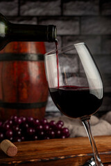 glass of red wine with a bottle of wine, falling into it with a wooden background and grapes