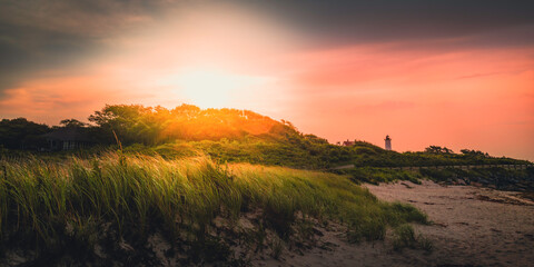Bright sun rising over the dark green forest hill with dramatic pink and purple clouds in Woods Hole on Cape Cod, Massachusetts.