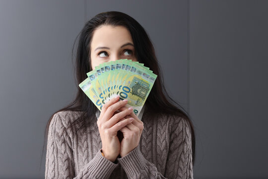 Young pensive woman holding lot of euro bills in front of her