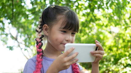 Little beautiful girl with pink hair using the phone outdoors. Kids and Technology, smartphone, e-learning
