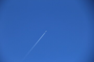 くっきりと飛行機雲を描きながら、飛行機が青空を飛ぶ風景