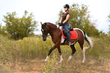 Girl rides a pinto horse at a trotting in the field