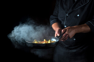 Chef prepares vegetables in a frying pan. Cooking healthy vegetarian food and meal on a dark background. Free advertising space