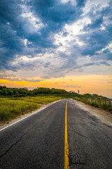 Dramatic cloudscape over the two-lane coastal road along the beach wild plants in Woods Hole on Cape Cod, Massachusetts.