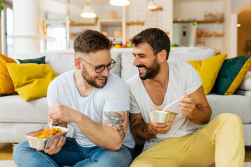 Attractive happy married hipster couple sitting on the floor in the living room and eating pasta for dinner. - 456817516