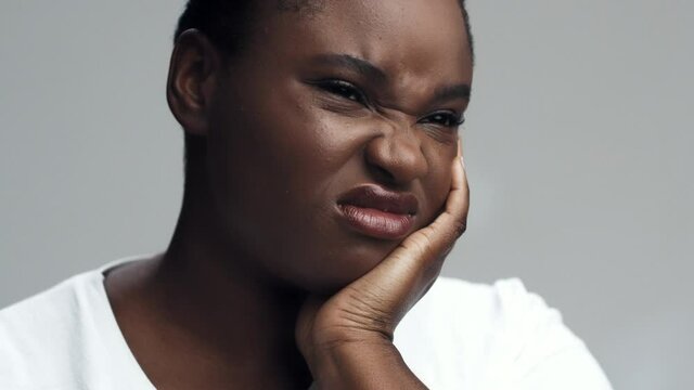 Unhappy african american woman suffering from acute tooth pain, touching her cheek and grimacing, close up portrait