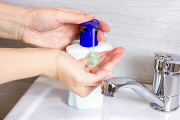 Young caucasian woman washes hands with water and liquid antiseptic soap in the bathroom.
