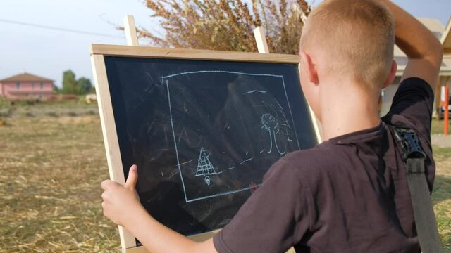 Close-up school child draws a treasure map on the blackboard while being in nature. Glamping nearby.