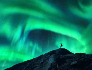 Fotobehang Northern lights and silhouette of standing woman with raised up arms on the mountain. Aurora borealis and happy girl. Sky with stars and green polar lights. Night landscape with aurora. Concept © den-belitsky