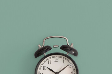 Black antique alarm clock on green background. Flat lay composition. Top view.