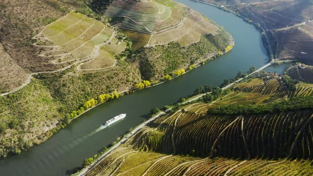 Drone shot of cruise ship moving along Douro river, Peso da Regua, Vila Real, Portugal, Europe. Scenic view of vineyard terraces covered green mountains. Tourist boat traveling in green landscape, 4k