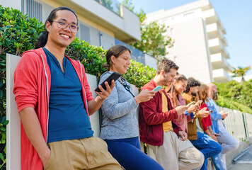 multiethnic group of friends in the street outdoors interacting with smartphones on social media laughing and having fun. diverse people together on happy holidays. technology and lifestyle concept