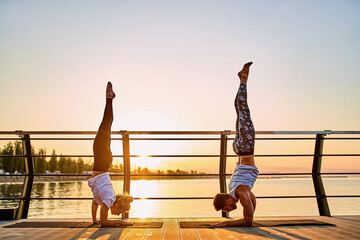Couple practicing acrobatic yoga together, doing Handstand pose on nature outdoors at sea.