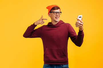 stylish young guy in an orange hat with glasses and a red sweater guy rejoices at a message on the phone