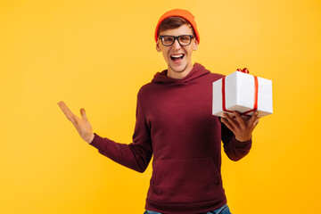 joyful young guy in an orange hat with glasses and a red sweater delighted with his gift, festive mood