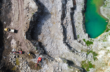 Aggregate mine with heavy machinery, excavators and tipper loaders in aerial shot. Working quarry...