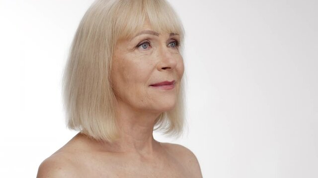 Beauty of aging. Semi profile portrait of senior blonde woman looking aside, white studio background, empty space