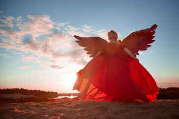A plump blonde middle-aged woman with red angle wings in a desert with dunes and sand in a nice...