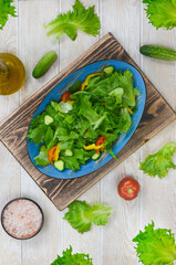 fresh summer green salad with vegetables cucumber, tomato, bell pepper, and leaf lettuce in ceramic bowl, dieting and vegan food on wooden background