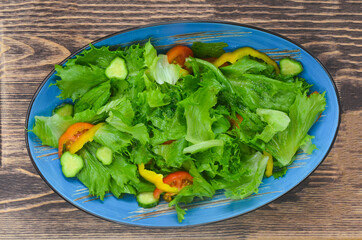 fresh summer green salad with vegetables cucumber, tomato, bell pepper, and leaf lettuce in ceramic bowl, dieting and vegan food on wooden background
