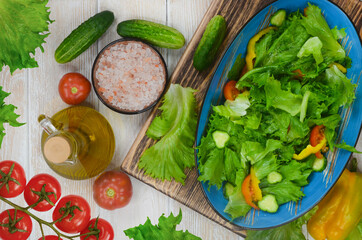 fresh summer green salad with vegetables cucumber, tomato, bell pepper, and leaf lettuce in ceramic bowl, dieting and vegan food on wooden background