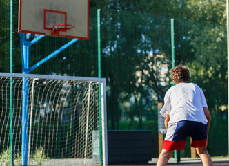 Cute teenager plays basketball at city playground. A boy holds basketball ball in his hands outside. Active life, hobby, sports for children	