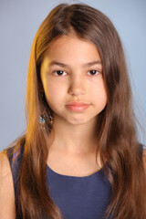 Fototapeta premium Close-up portrait of a beautiful dark-haired teenage girl 12 years old in a blue dress. She looks carefully eye to eye.