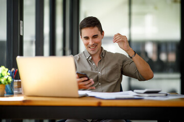 Portrait of Happy excited successful young businessman or handsome man triumphing in office,businessman working on laptop computer.