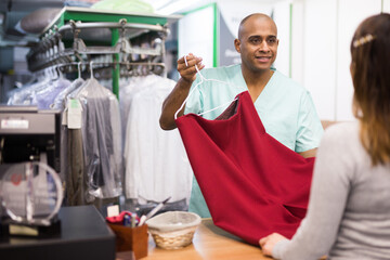 Fototapeta na wymiar Portrait of dry cleaning employee at work, man giving clean clothes to client