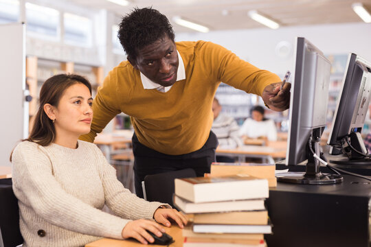 Portrait of confident man librarian assisting woman in library