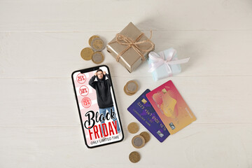 Black Friday advertising on screen of mobile phone, gift and money on white wooden background