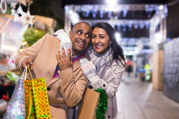 Naklejka premium Happy married couple with packages of gifts at new year street fair