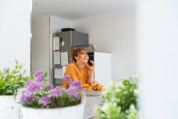 caucasian female in an orange shirt talking on the phone in a kitchen