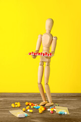 Wooden mannequin with pills on color background