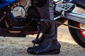 Closeup shot of a male's boot in front of a motorcycle