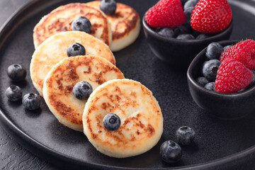 Close-up of cottage cheese pancakes with fresh with strawberry and blueberries on dark ceramic plate