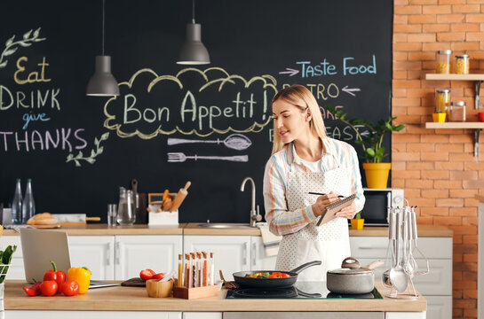 Young Housewife With Laptop Cooking In Kitchen At Home