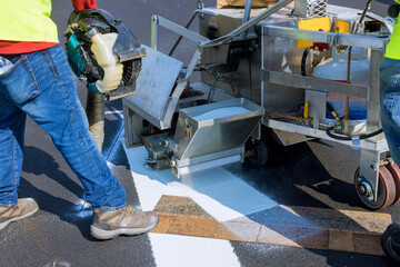 Workers apply a road marking to the stripe with white paint and sprinkle the stripes with a reflective powder on the asphalt