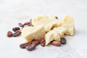 Pieces of cocoa butter and beans on light background