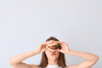 Young woman with tasty vegan burger on light background
