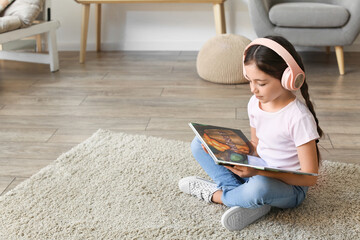 Little girl with headphones reading book at home
